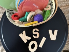 Methoden: Ein kleiner Korb auf einem schwarzen Tisch enthält bunte, laminierte Karten mit Begriffen wie Eingang und Website, sowie Holzbuchstaben. Auf dem Tisch liegen zusätzlich mehrere lose Holzbuchstaben verteilt.