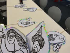 Methoden: Auf einem langen Tisch liegen mehrere ausgeschnittene schwarz-weiße Zeichnungen abgebildet, die auf Holzspieße geklebt wurden. Bei diesen handelt es sich um die Illustrationen von Kerstin Recker. Zwei von ihnen werden direkt vor die Kamera gehalten.