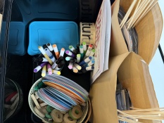 Methoden: In einer großen schwarzen Kiste liegen verschiedene Materialien, zum Beispiel bunte Marker in Bechern, laminierte farbige Karten, Holzbuchstaben, kleine Holzformen und weitere Utensilien in einem Korb.