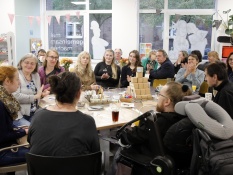 Methoden: Auf dem Bild sieht man eine größere Gruppe von Menschen aus dem Netzwerk die gemeinsam an einem Tisch im Projektbüro sitzen und fröhlich wirken. Auf dem Tisch liegen Bastelmaterialien, Stifte, Papier, kleine Boxen und dekorative Elemente.